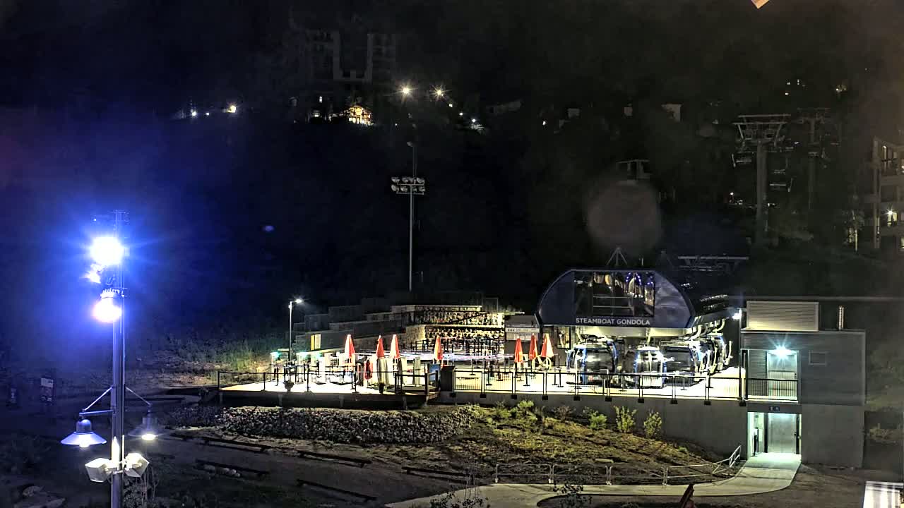 A gondola lift station with a building and outdoor seating area is illuminated at night.