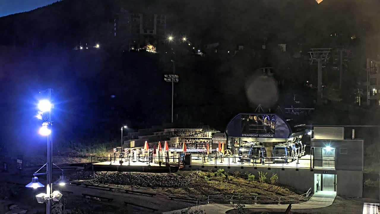 At night, a gondola station sits at the base of a dark mountain, illuminated by artificial lights.