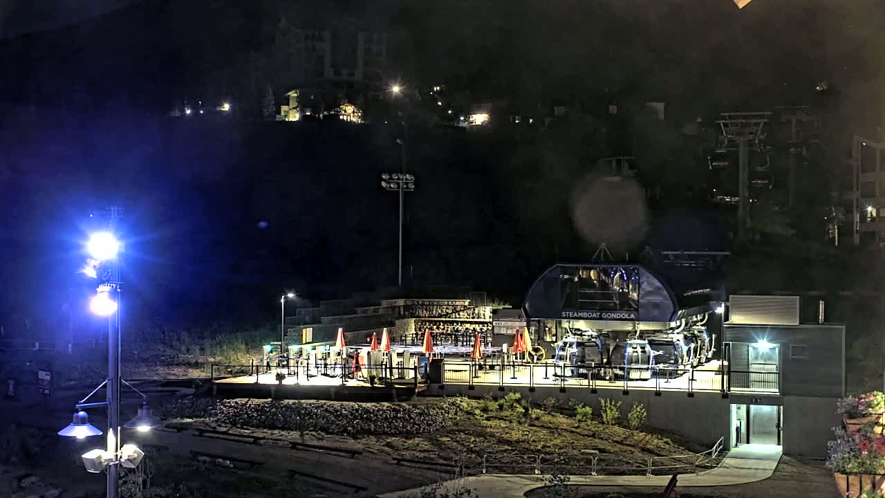 A gondola station, illuminated at night, sits at the base of a dark, tree-covered hill.