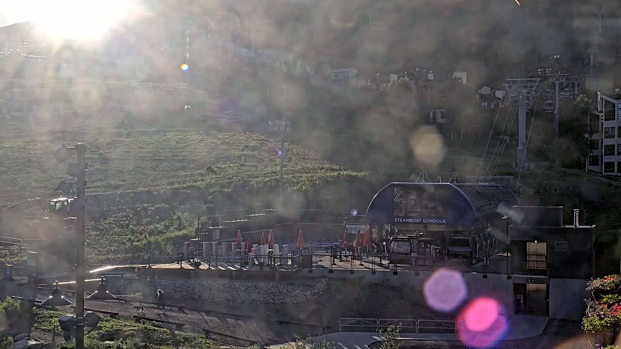 A gondola station sits on a hillside, partially obscured by hazy sunlight and lens flare.