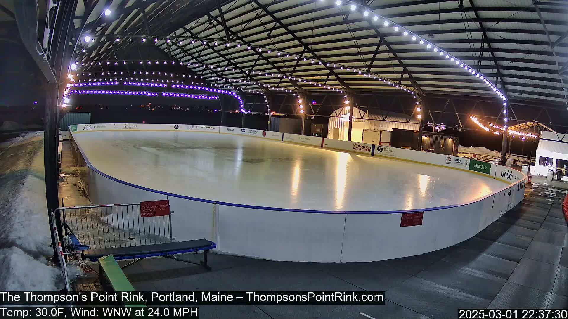 An outdoor ice rink under a covered structure is illuminated at night, with a 30°F temperature and a 24 mph wind from the west-northwest.