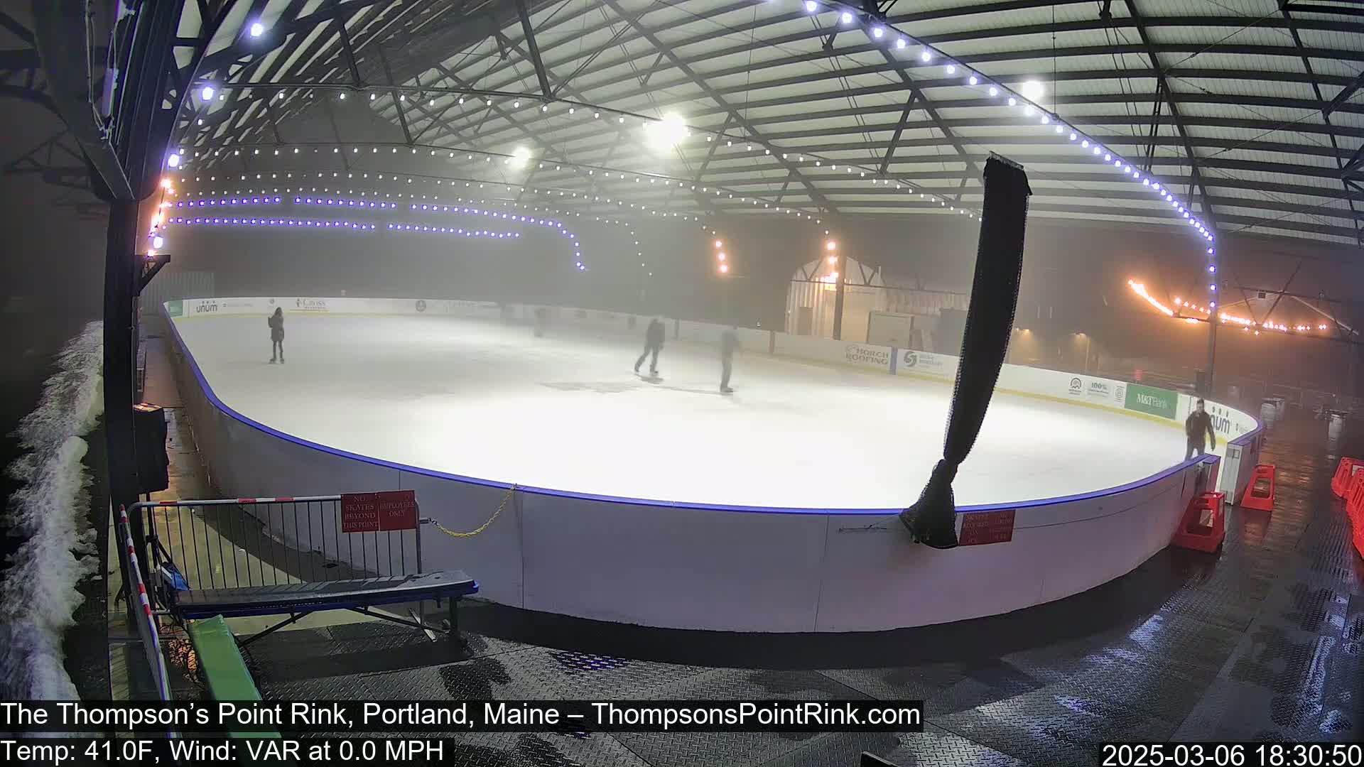 A foggy outdoor ice rink with several people ice skating inside.