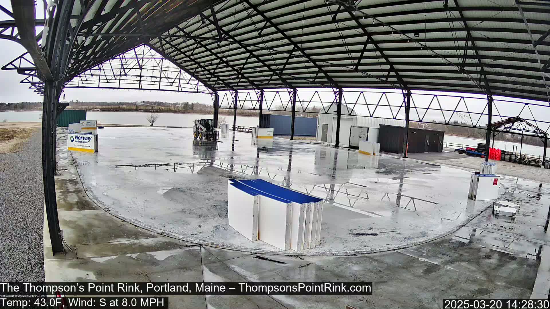 A wet, open-air rink under a metal roof on an overcast day.