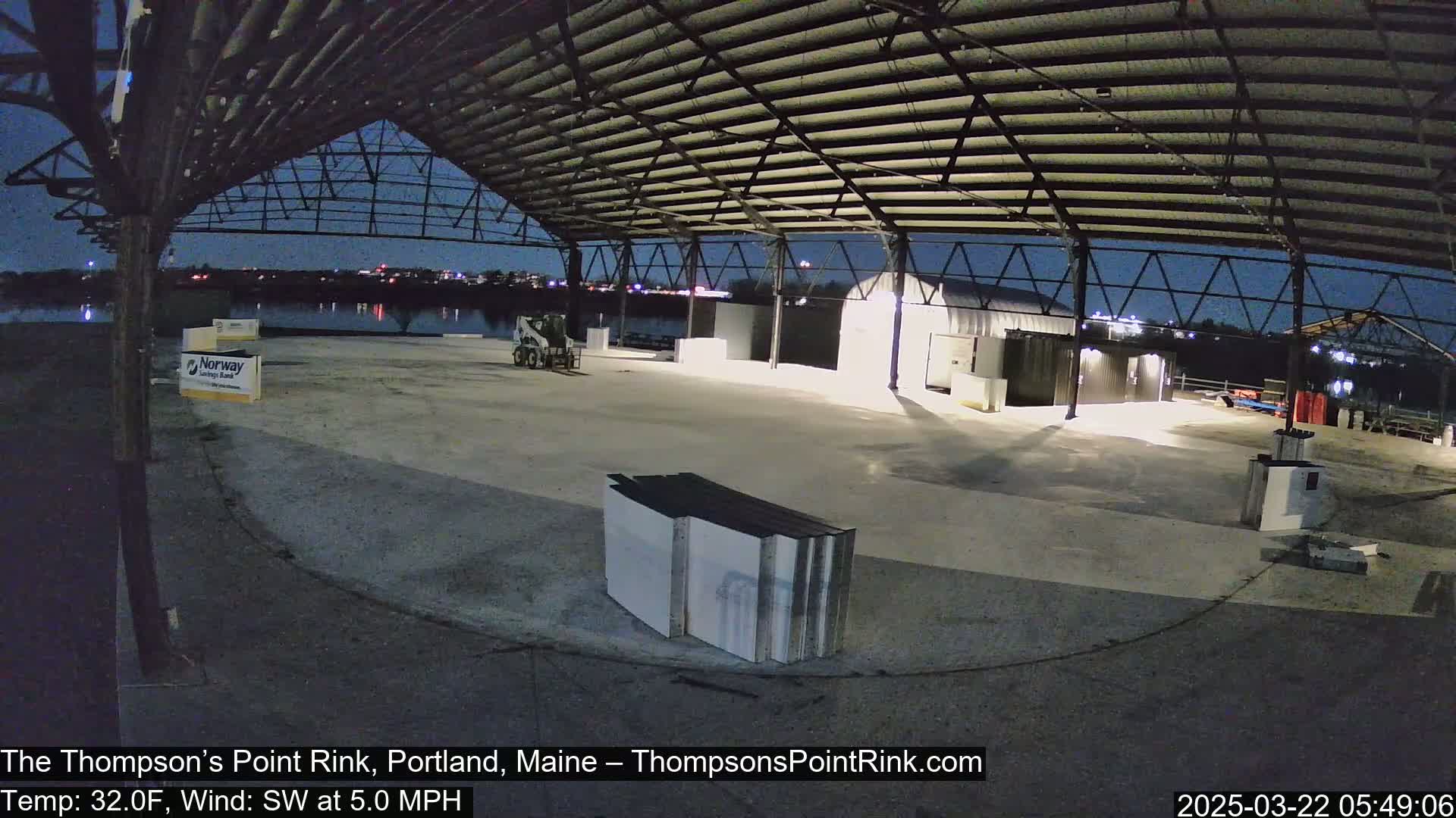 An empty, open-air rink under a metal framework at night with calm weather.