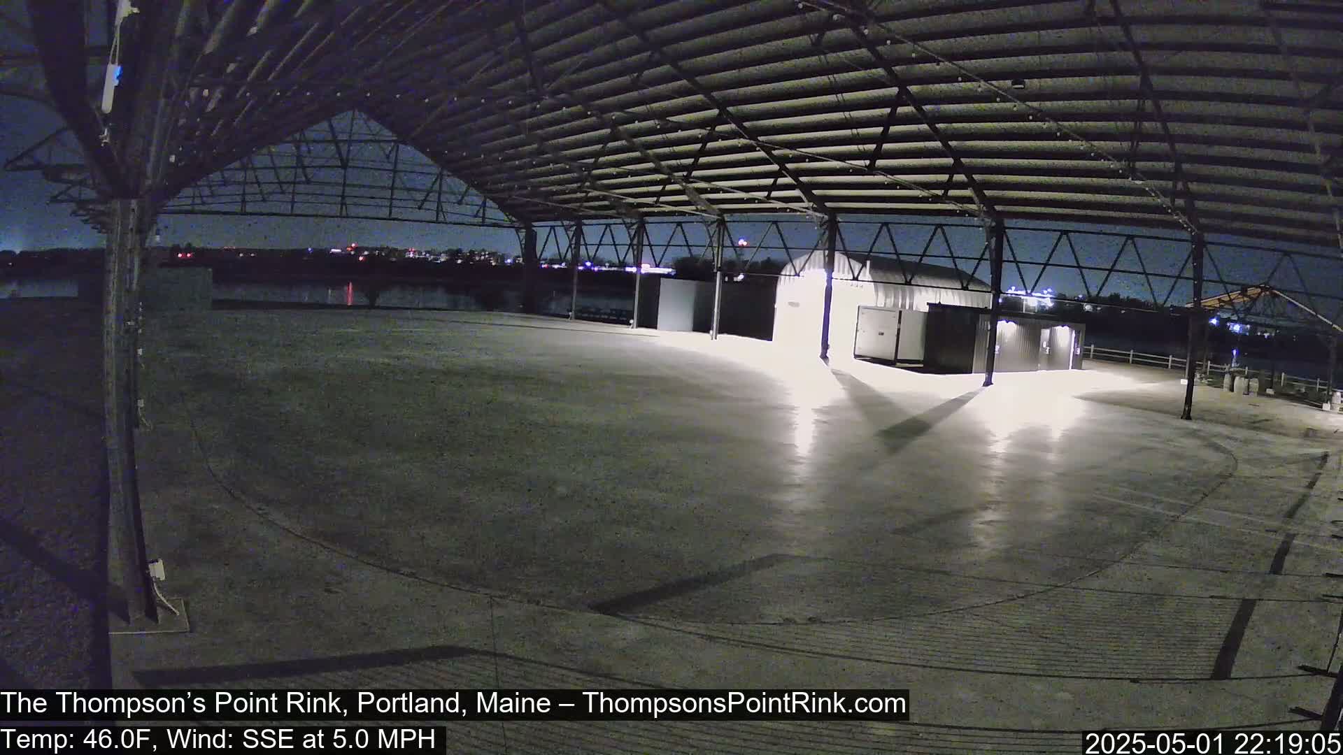 An empty, open-air rink under a metal framework at night, with a calm wind blowing from the south-southeast.