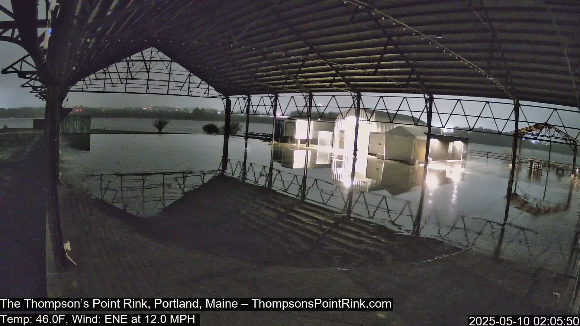Under a dark, overcast sky, a flooded rink sits beneath a metal-framed structure.