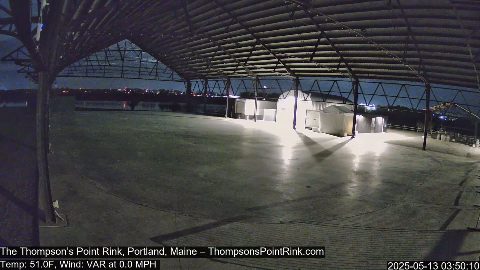 An empty, brightly lit concrete area is enclosed by a large metal structure under a nighttime sky.