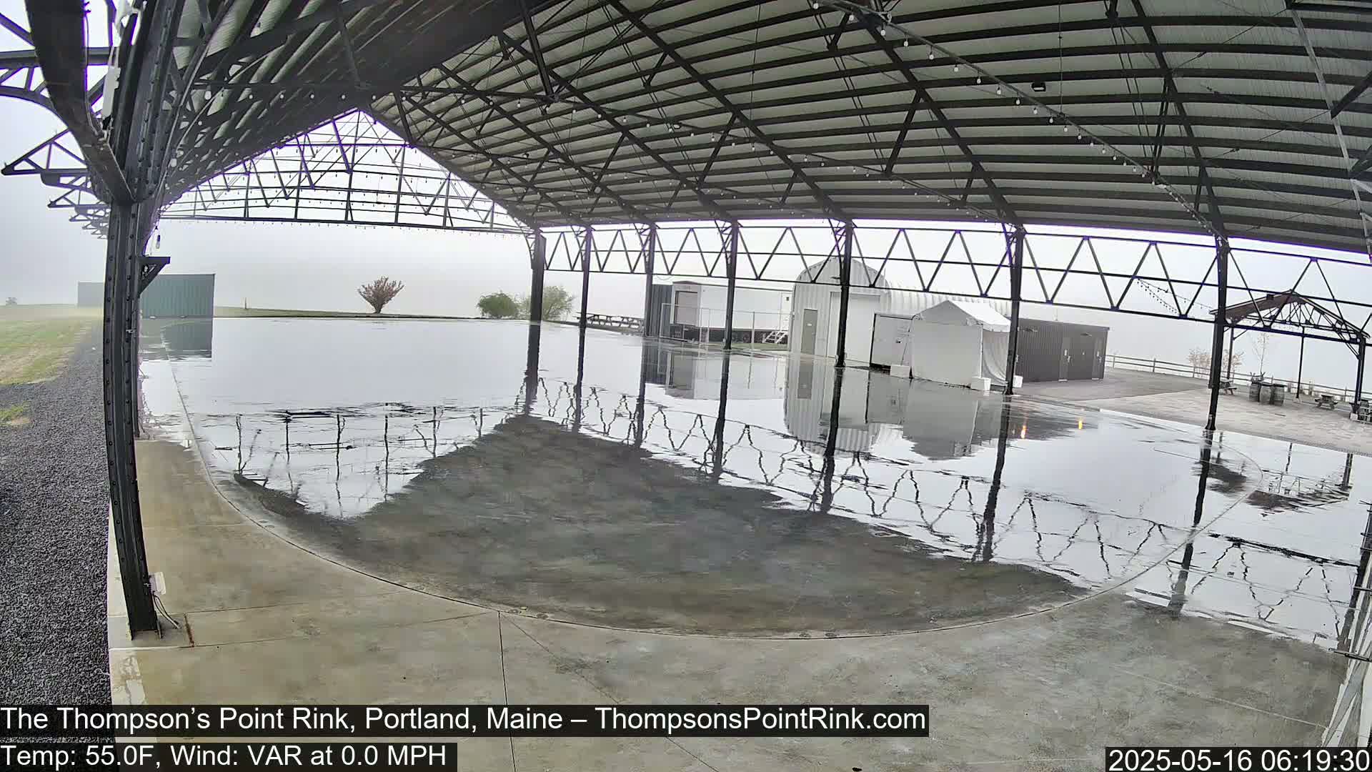 A wet, open-air rink sits under a metal roof in foggy conditions.