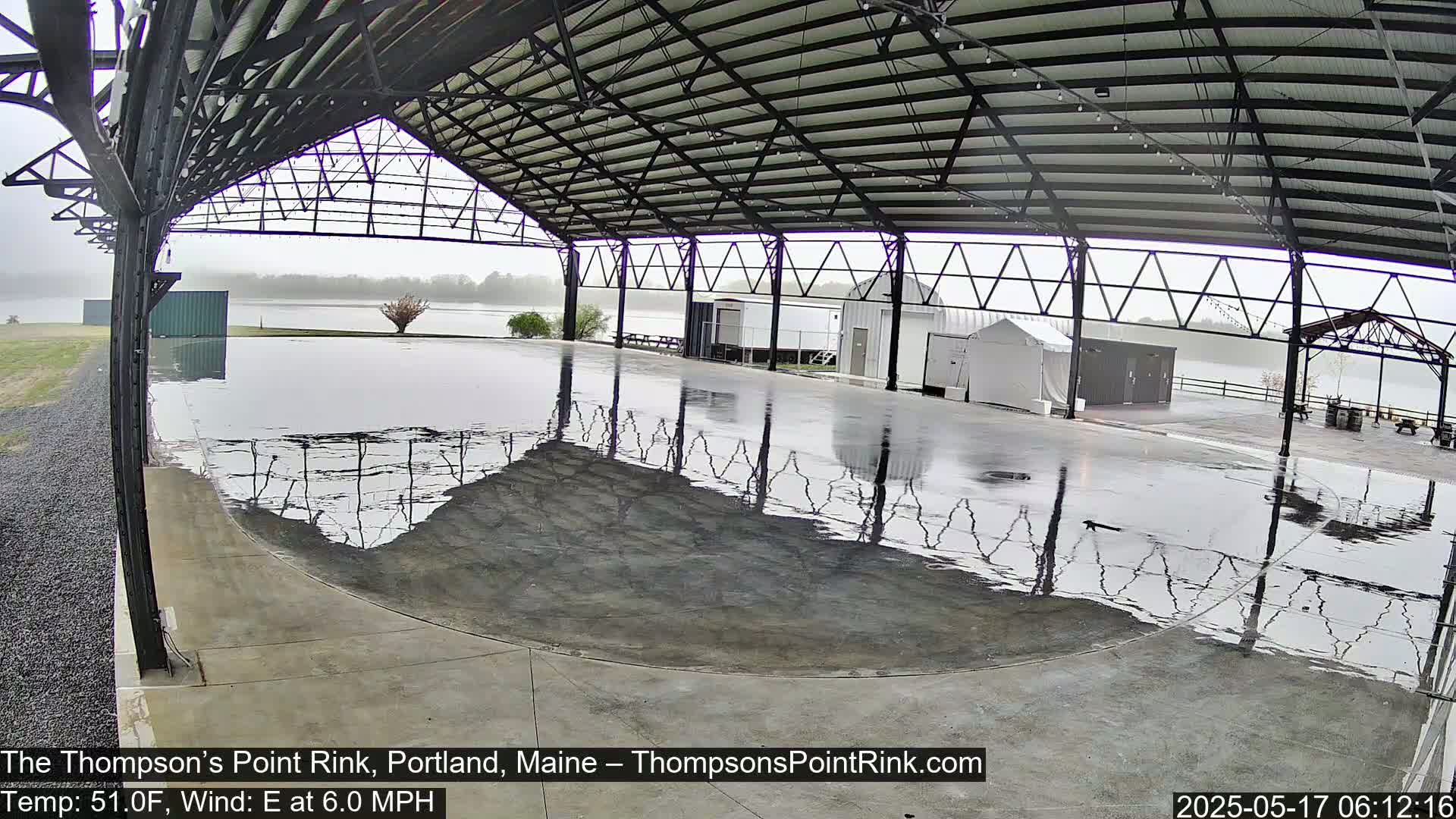 A wet, open-air rink under a metal framework, with a calm body of water visible beyond.