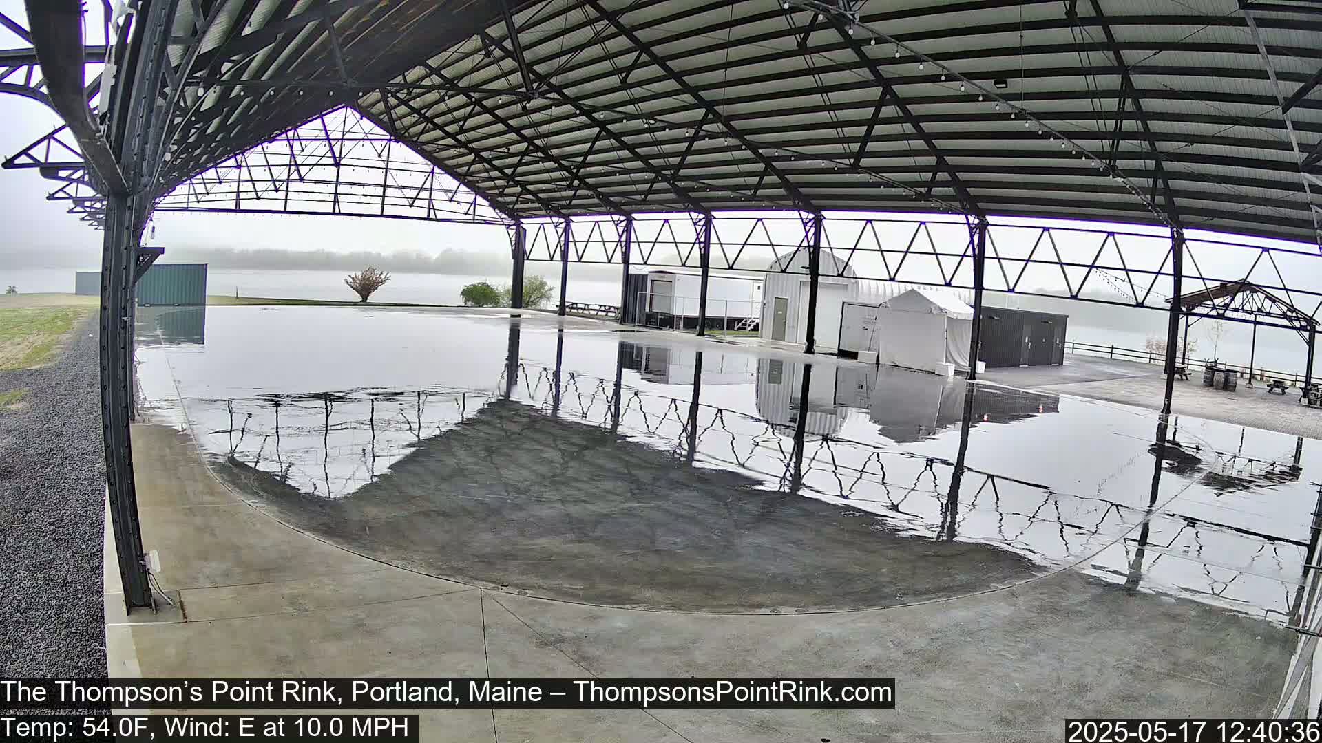 A wet, open-air rink under a metal framework on an overcast day.