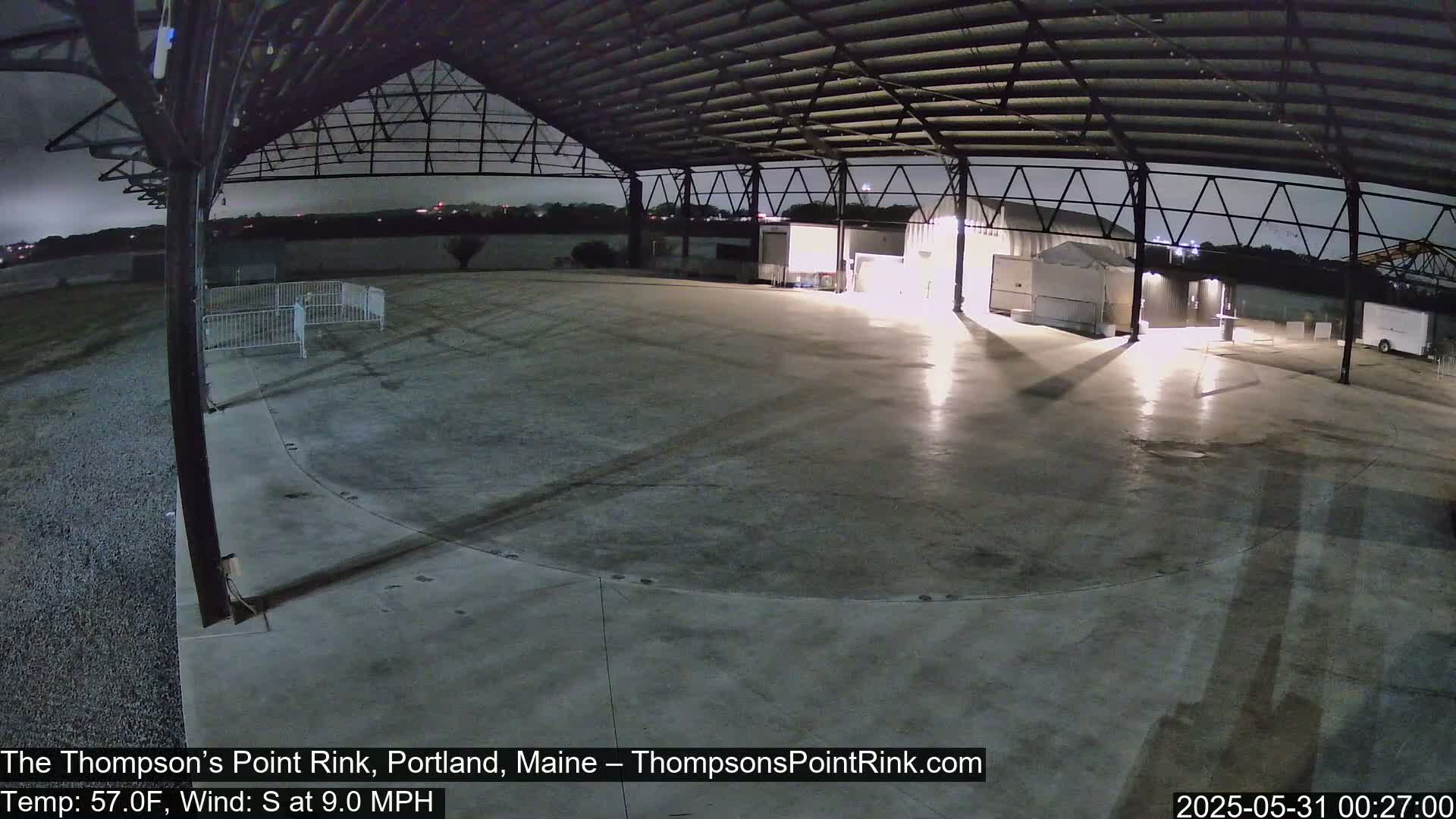 A large, empty, concrete area under a metal-roofed structure at night, with a slight south wind.