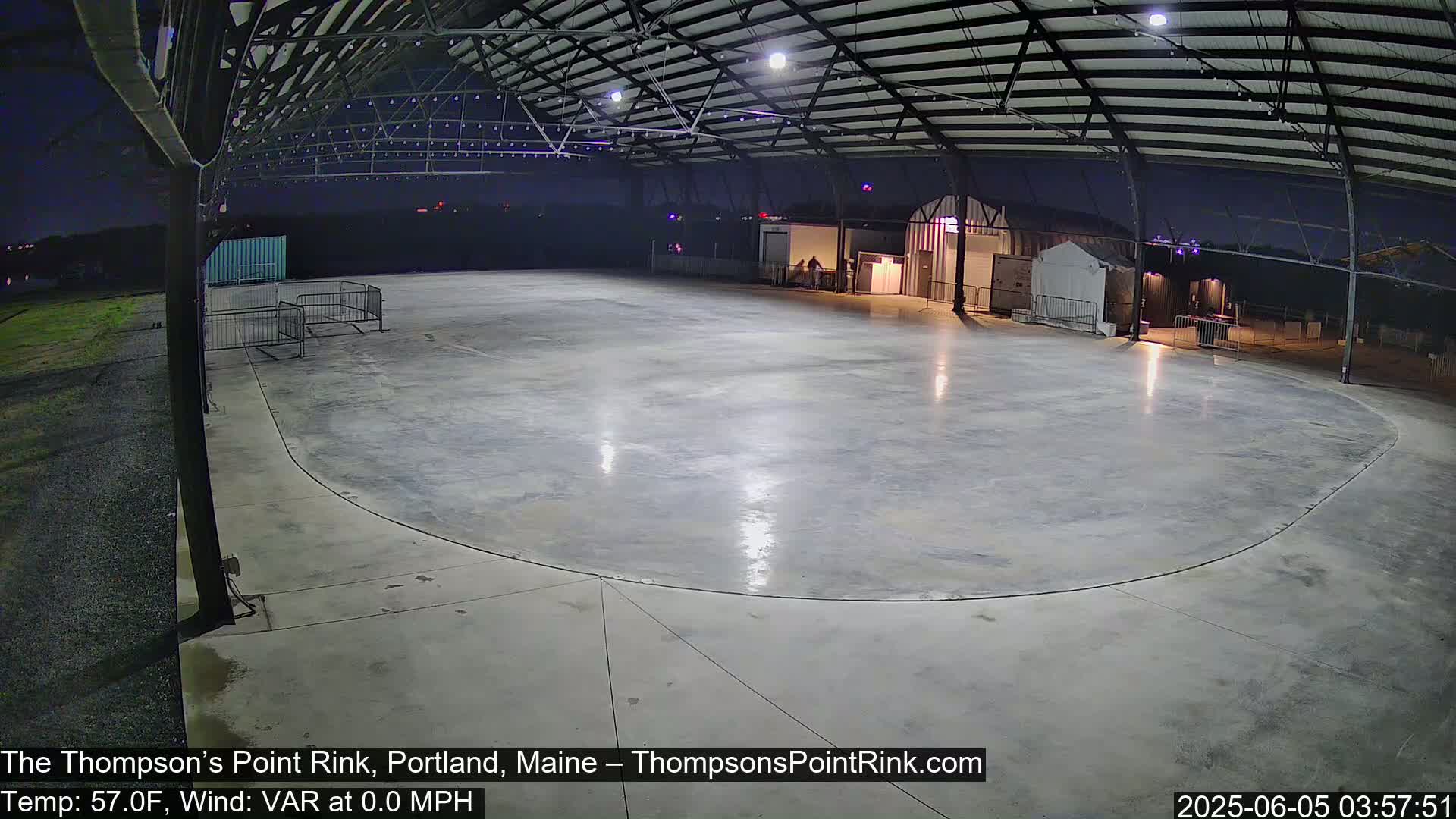 An empty, oval-shaped concrete rink sits under a metal roof at night, illuminated by artificial lights.