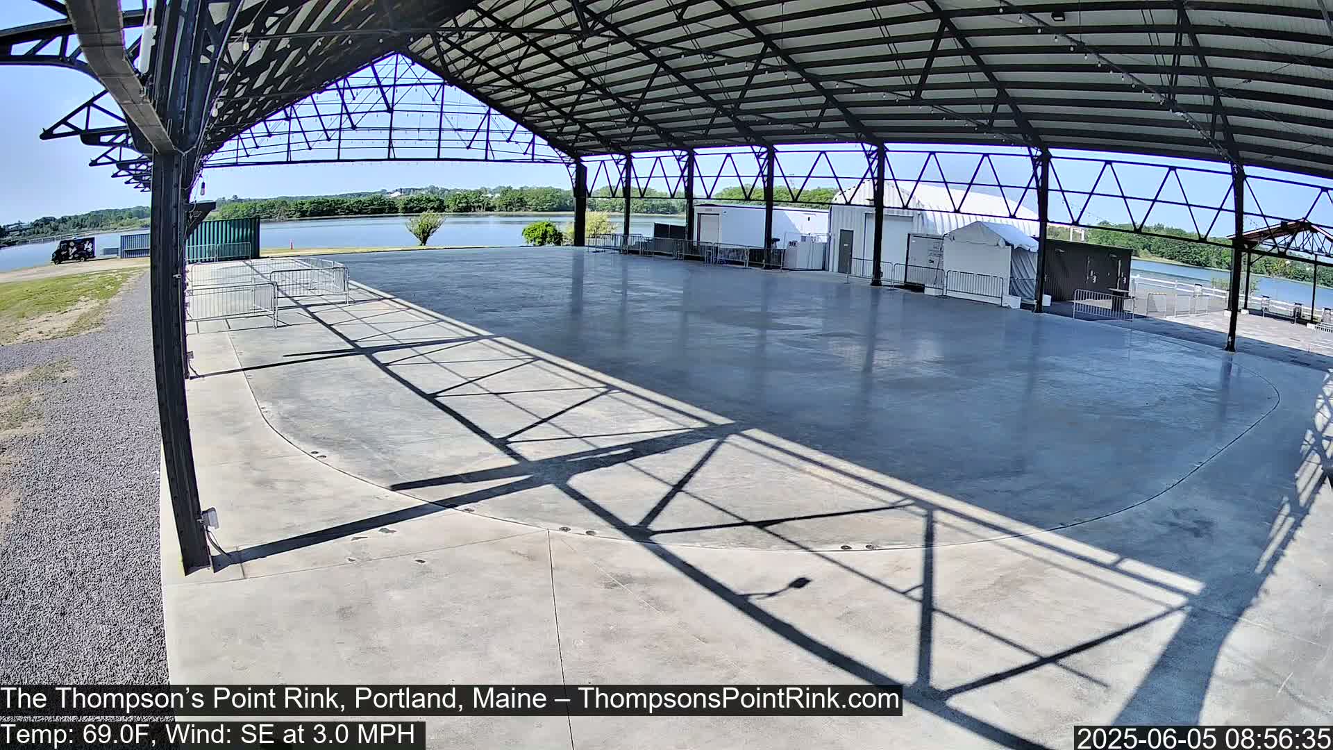 A large, empty paved rink sits under a metal roofed structure on a sunny day with a gentle southeast wind.