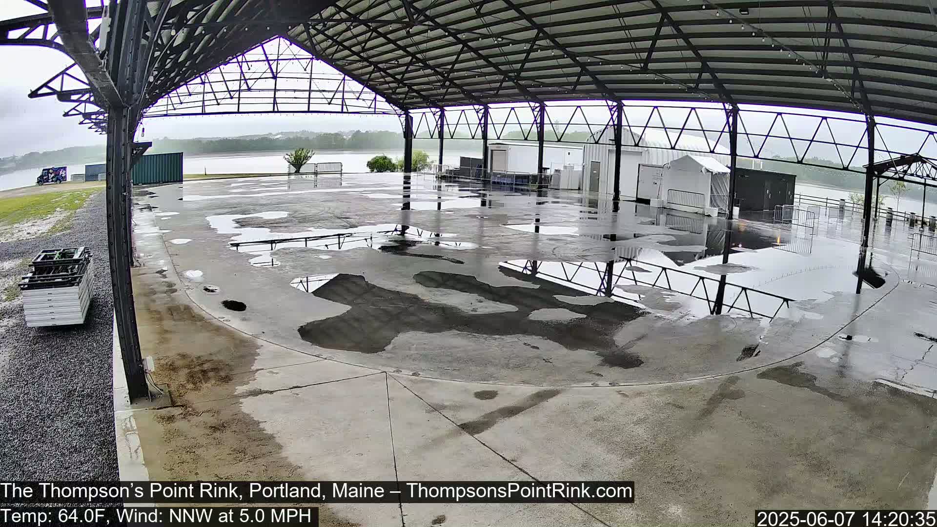 A wet, open-air rink under a metal roof during a light rain.