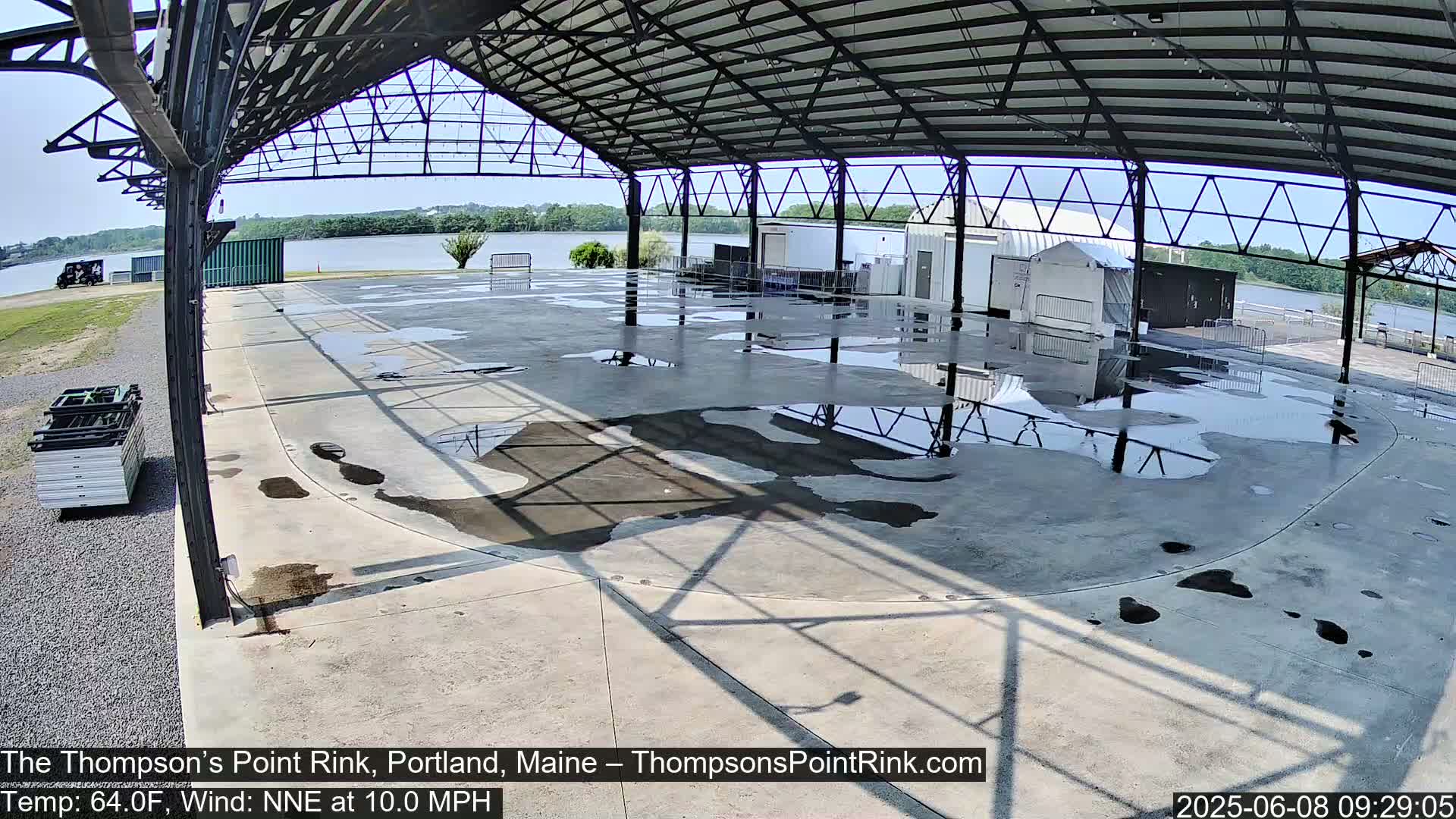 A wet, open-air rink under a metal roof on a sunny day with a gentle wind.