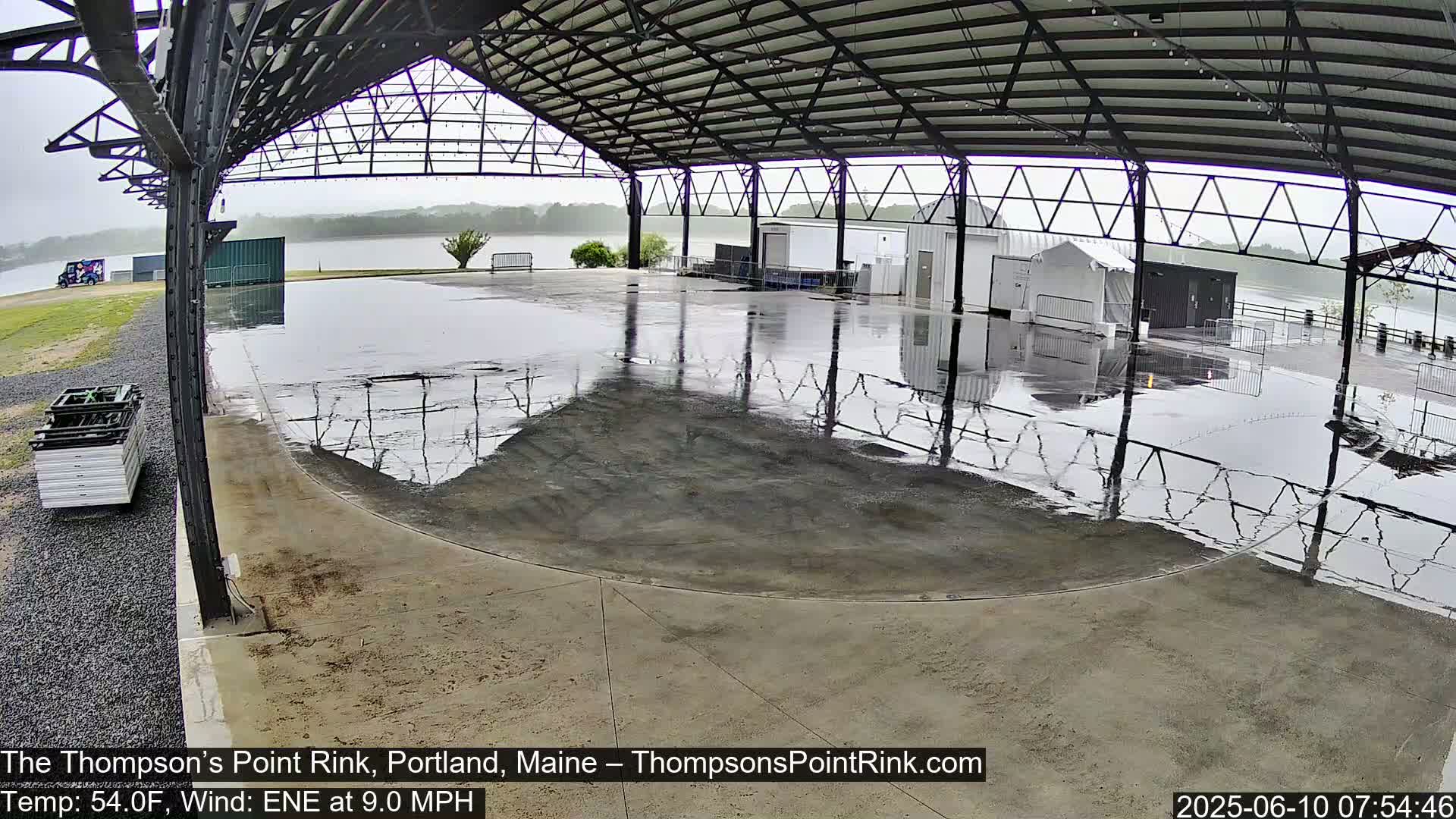 A wet, open-air rink sits under a metal roof during rainy weather.
