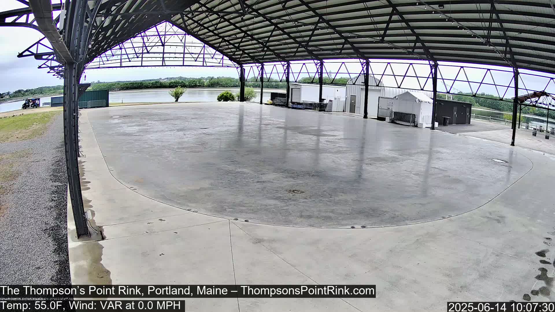 A large, empty, concrete rink sits under a metal roofed structure on an overcast day.