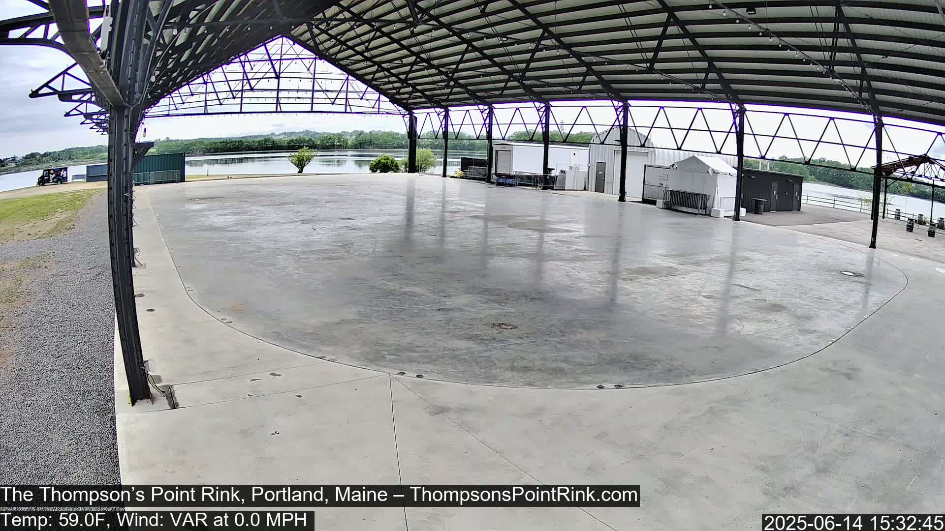 A large, empty, concrete rink sits under a metal roofed structure on an overcast day.