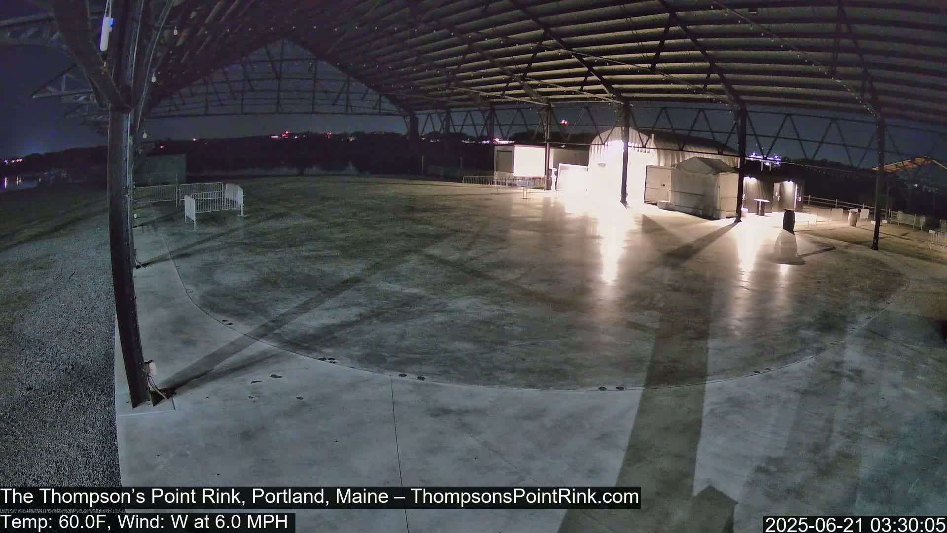 An empty, illuminated outdoor rink under a metal structure at night with a 60°F temperature and a 6.0 mph west wind.