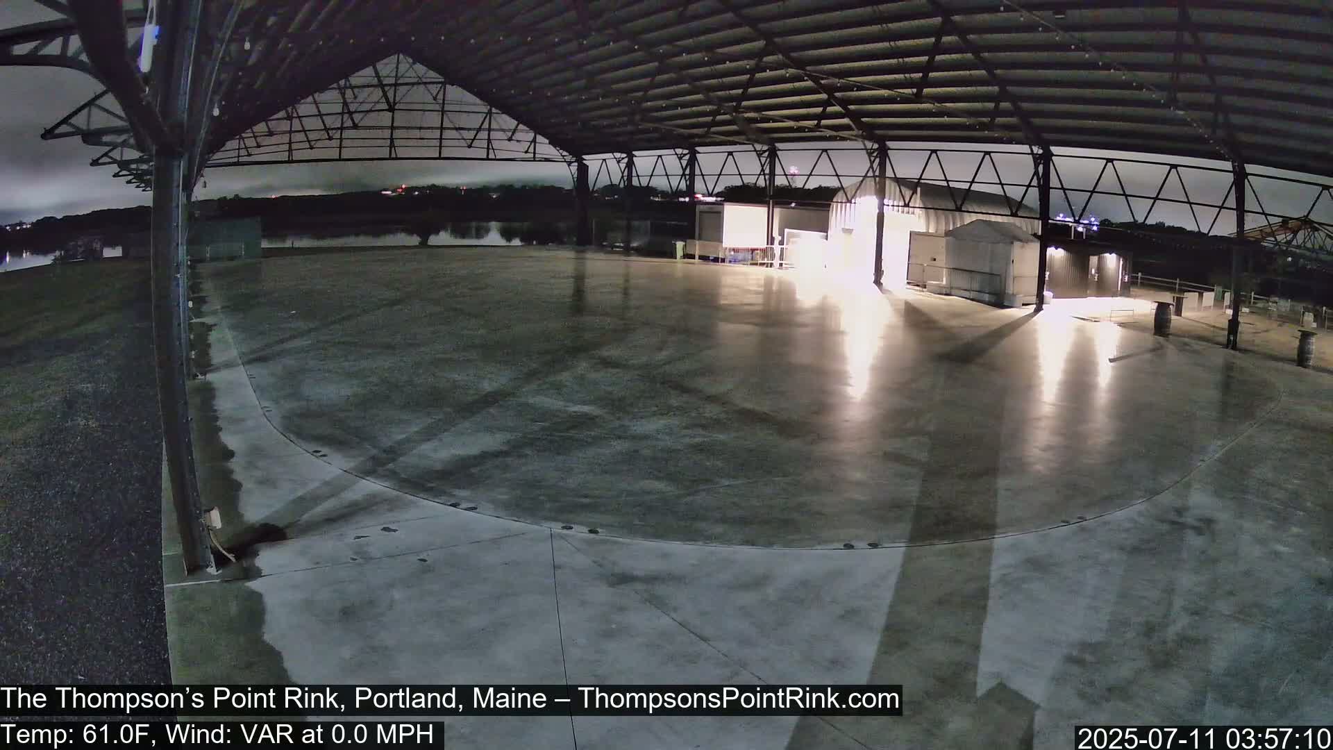 A large, empty, concrete rink under a metal roof at night, illuminated by several lights.