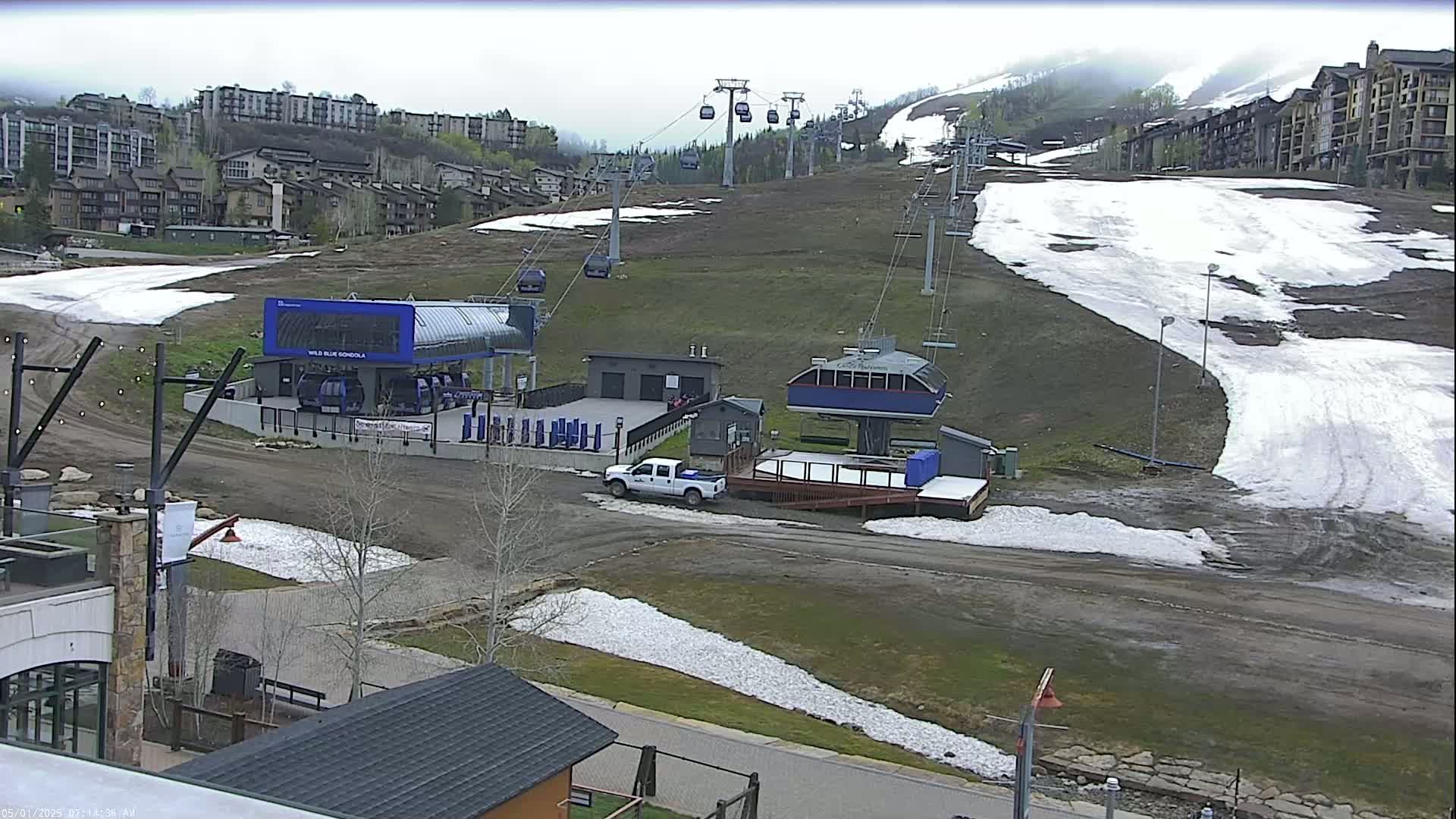 A ski resort with several chairlifts and a gondola station, partially covered in snow, under an overcast sky.