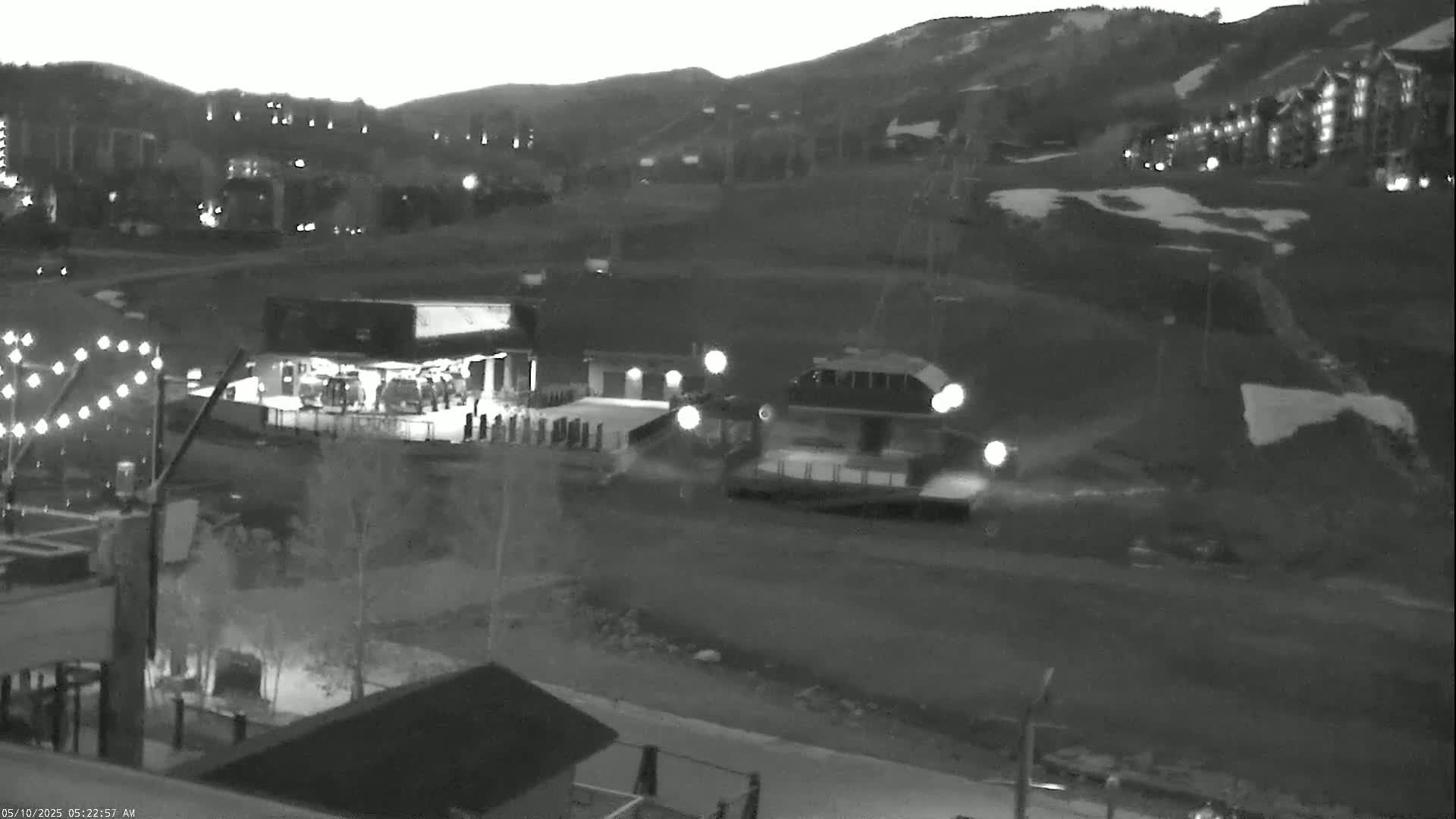 A nighttime, grayscale image shows a mountainside village with buildings and snowy slopes under a twilight sky.