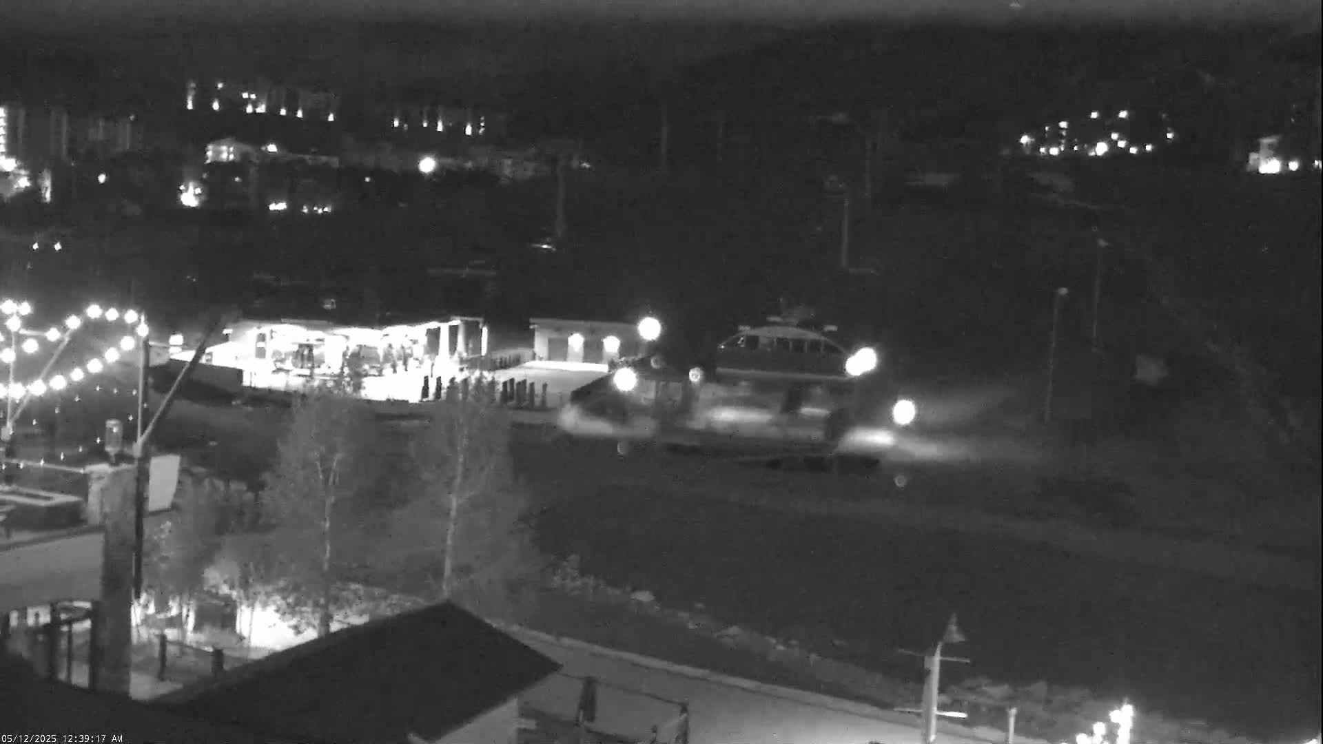 At night, a hovercraft moves across a snow-covered area near buildings with lights on, under a dark sky.