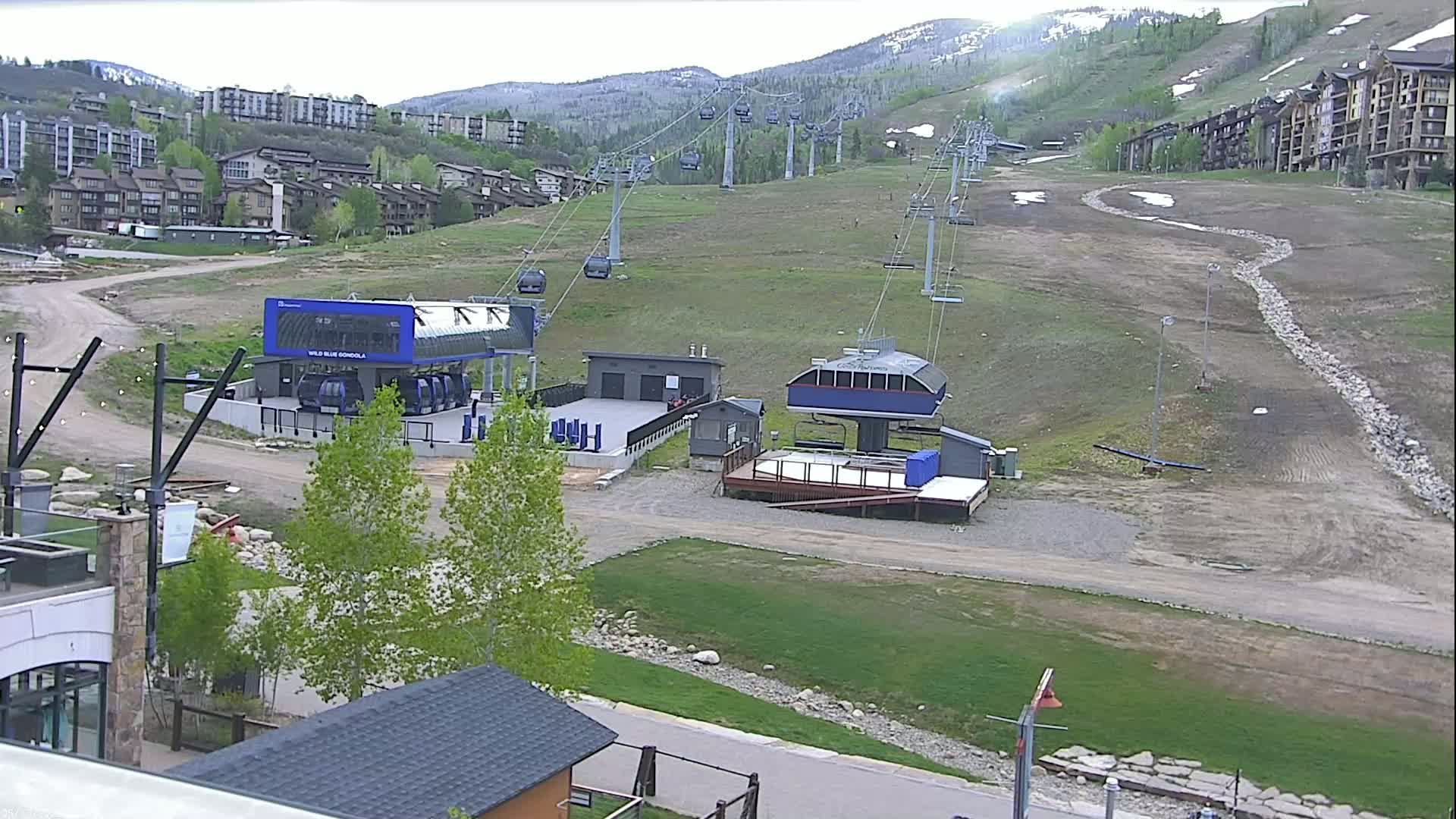 A mostly clear day reveals a ski resort with chairlifts, gondolas, and buildings, set against a backdrop of mountains.