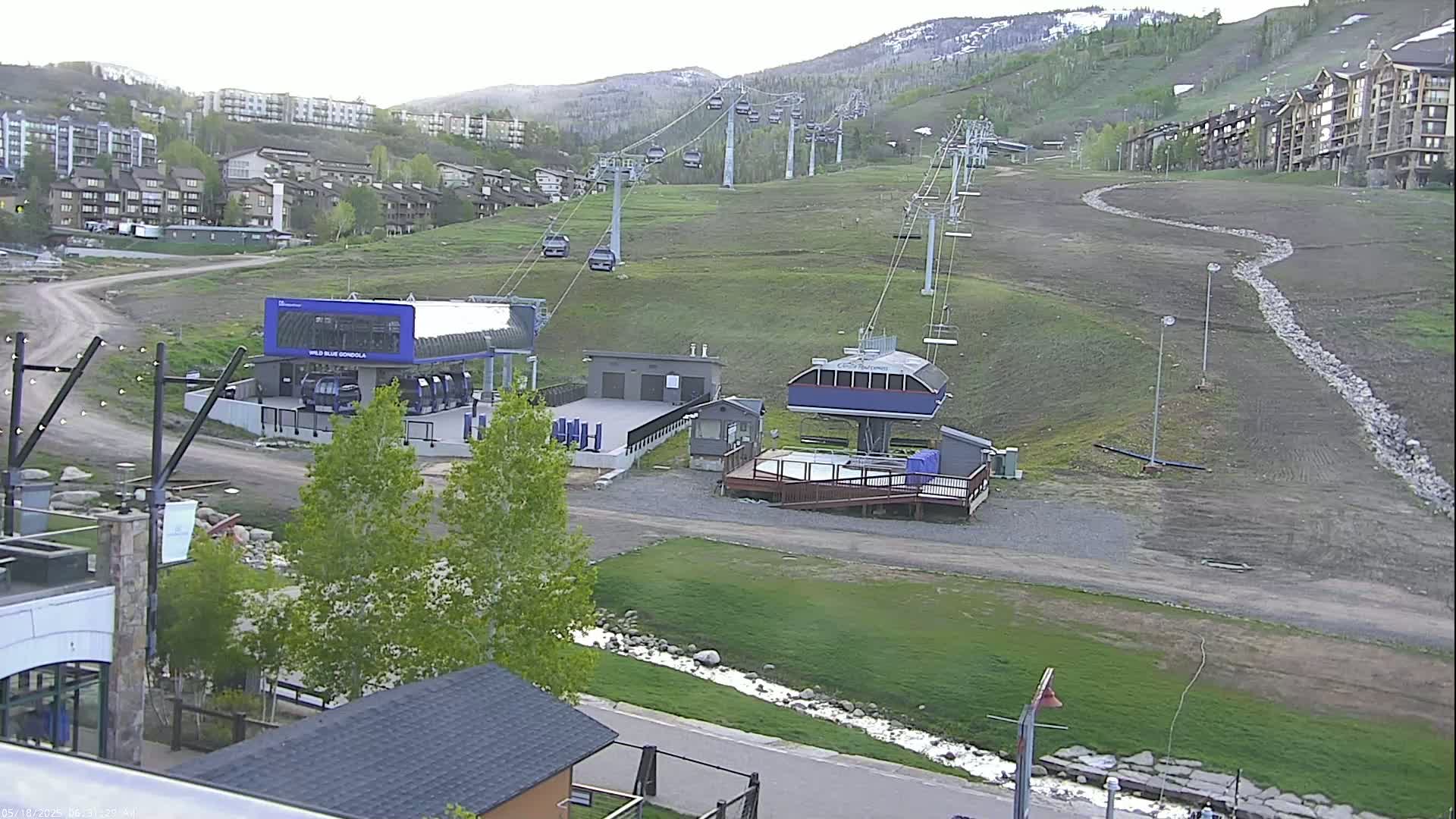 A ski lift and gondola station are situated on a grassy hill overlooking a residential area under a mostly clear sky.