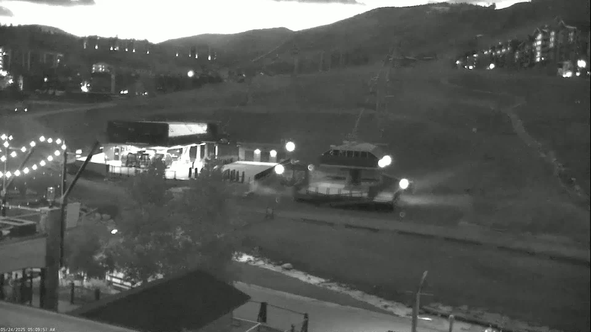 A nighttime infrared image shows a ski resort scene with a chairlift, buildings, and a few lights on, under mostly clear skies.