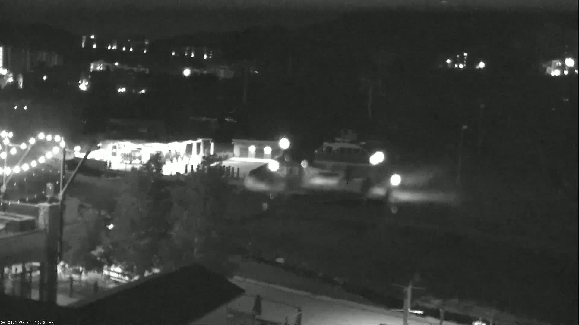 A nighttime, low-light view of a parking lot with several vehicles and illuminated buildings, showing a string of lights in the lower left corner.