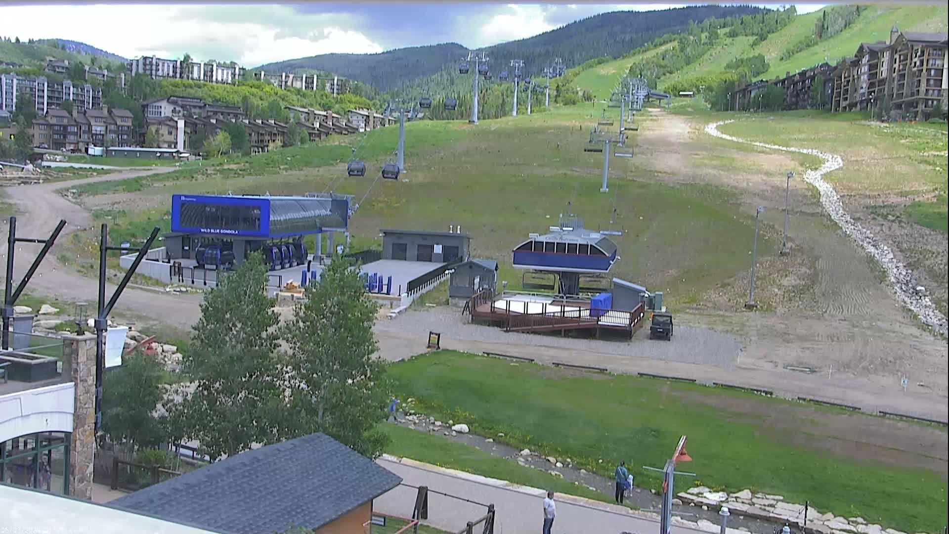A ski resort in the summer, showing chairlifts, buildings, and grassy slopes under partly cloudy skies.