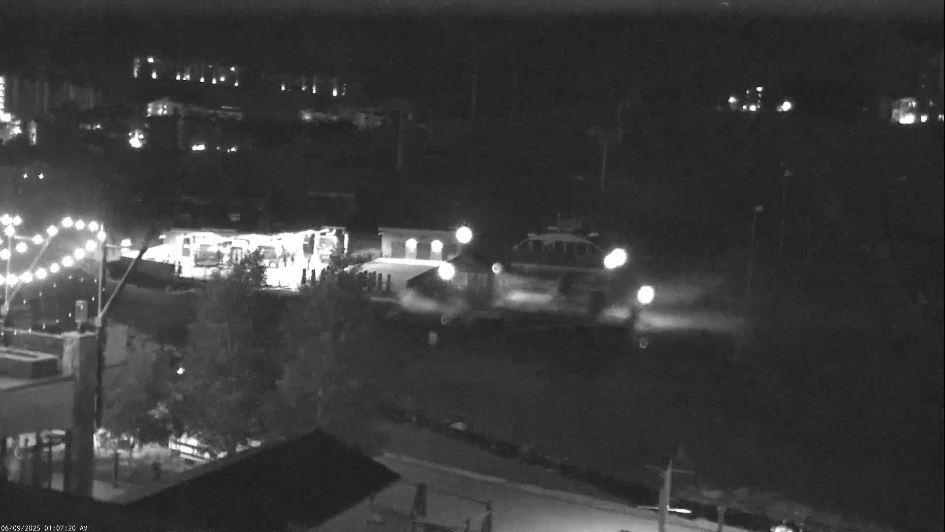 A nighttime, low-light view shows several vehicles near buildings and streetlights.