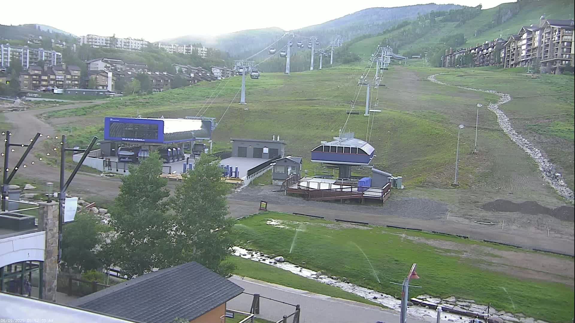 A ski resort base area with several chairlifts extending up a grassy mountainside under an overcast sky.
