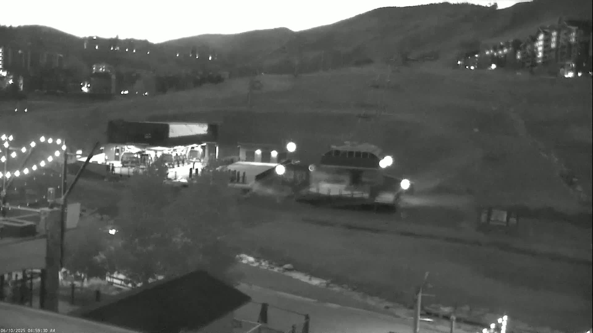 A nighttime, grayscale image shows a mountainside village with buildings and lights, under a dusky sky.