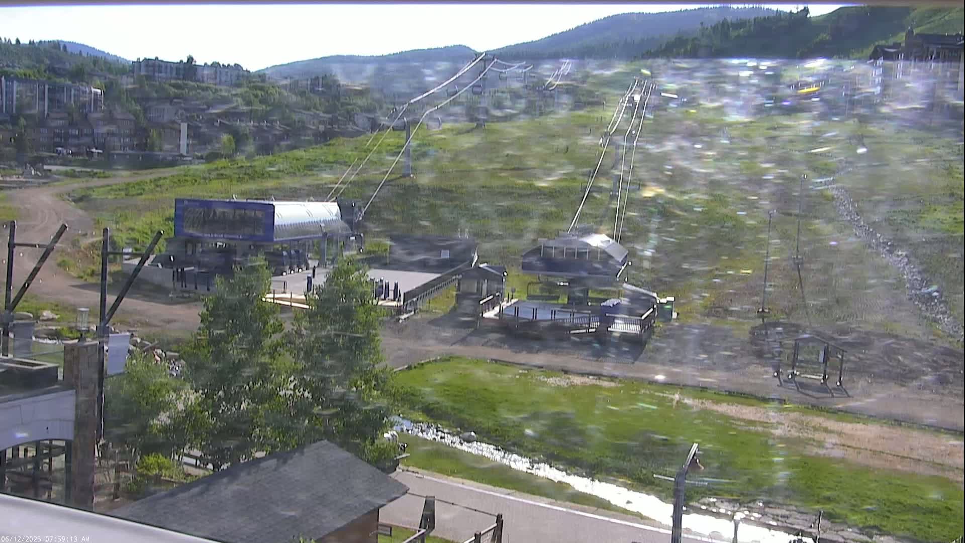 A ski lift and its base stations are visible on a grassy hillside under hazy, windy conditions.