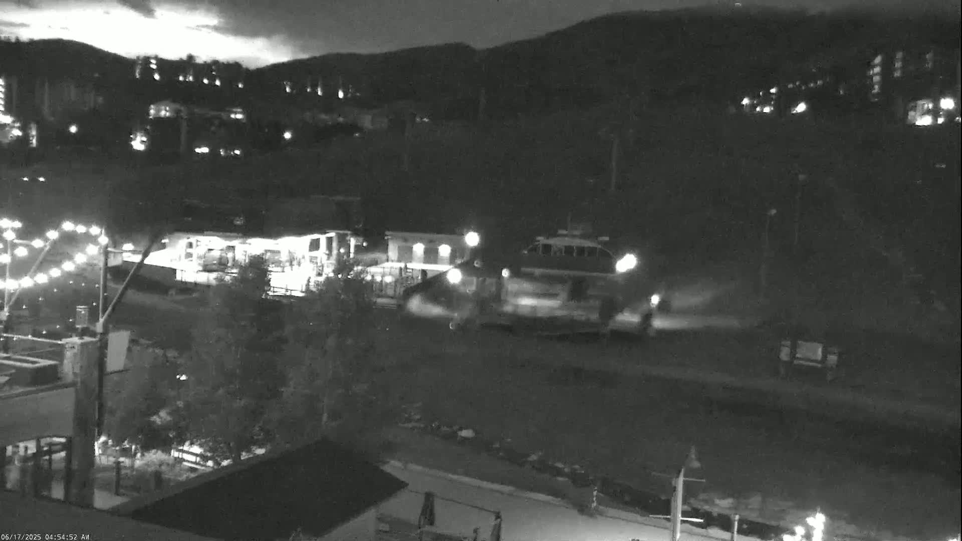 A nighttime, low-light view shows a vehicle moving through a town situated at the base of a mountain.