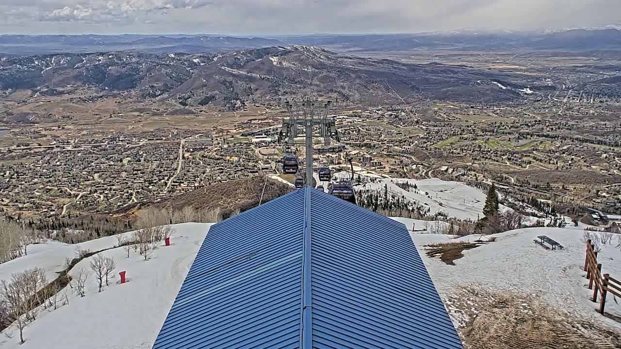 A blue roofed building overlooks a ski resort town nestled in a valley, with snow on the ground and partly cloudy skies.