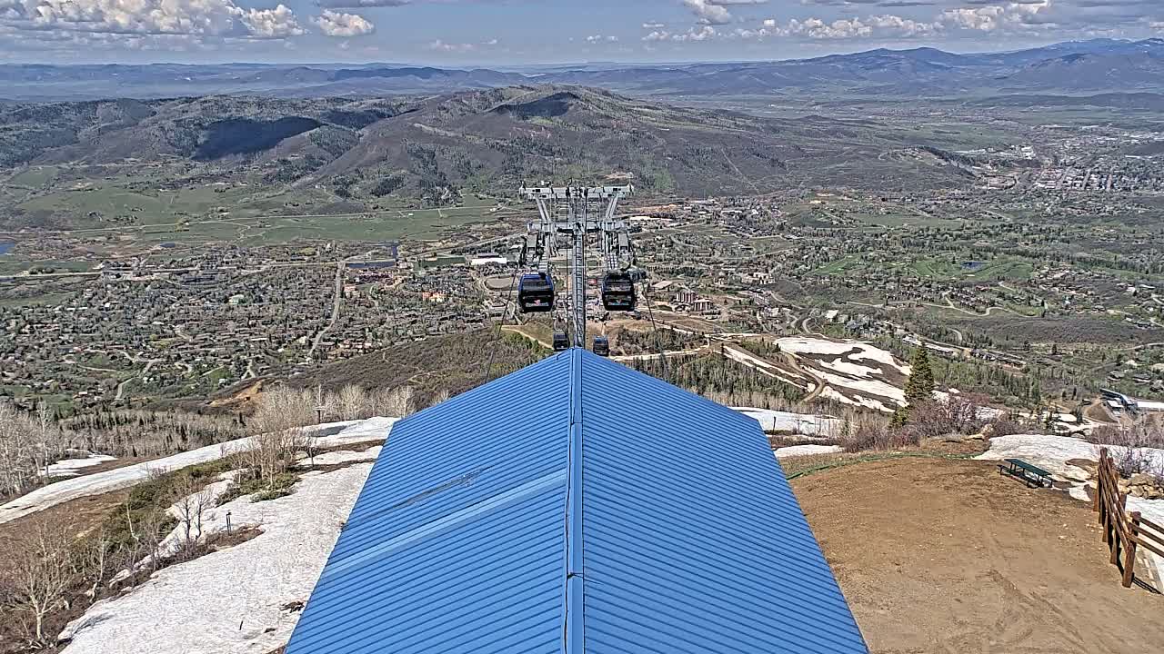 A blue metal roof overlooks a valley town with a chairlift in the distance on a partly cloudy day with patches of snow on the ground.