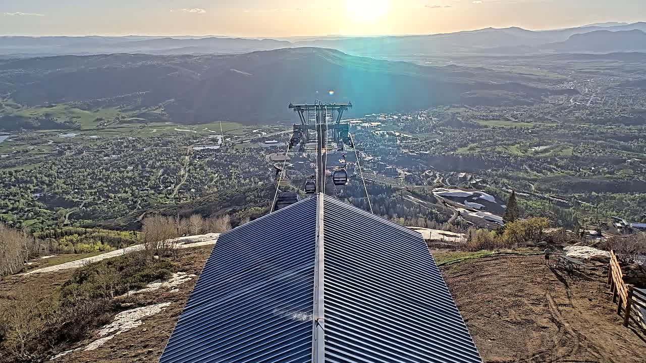 A chairlift ascends a mountain overlooking a valley town under a mostly sunny sky.