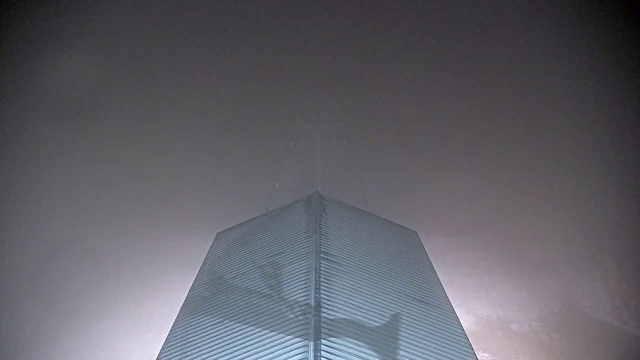 A tall, light-grey building with a triangular shape rises into a thick, foggy sky.