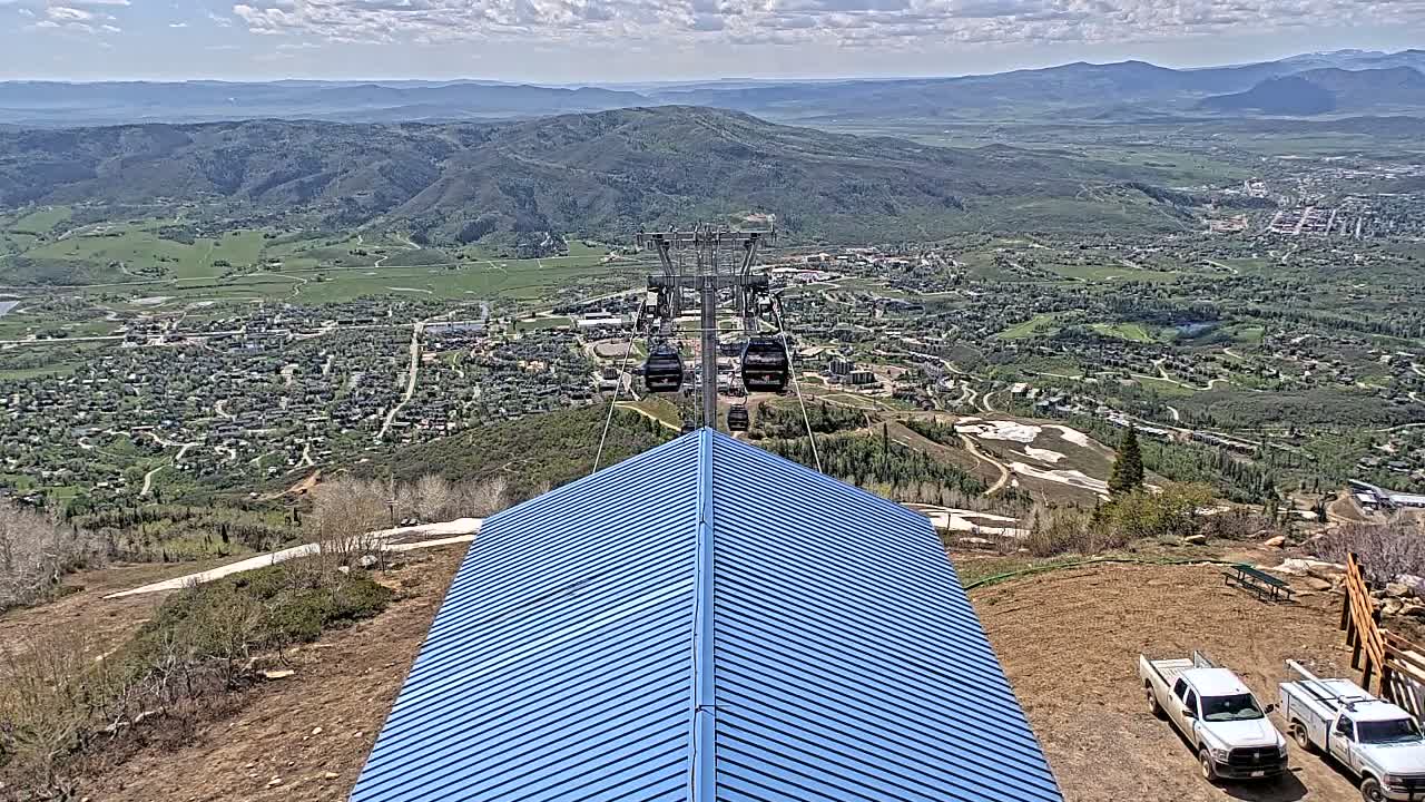 A chairlift ascends a mountain overlooking a town nestled in a valley on a partly cloudy day.