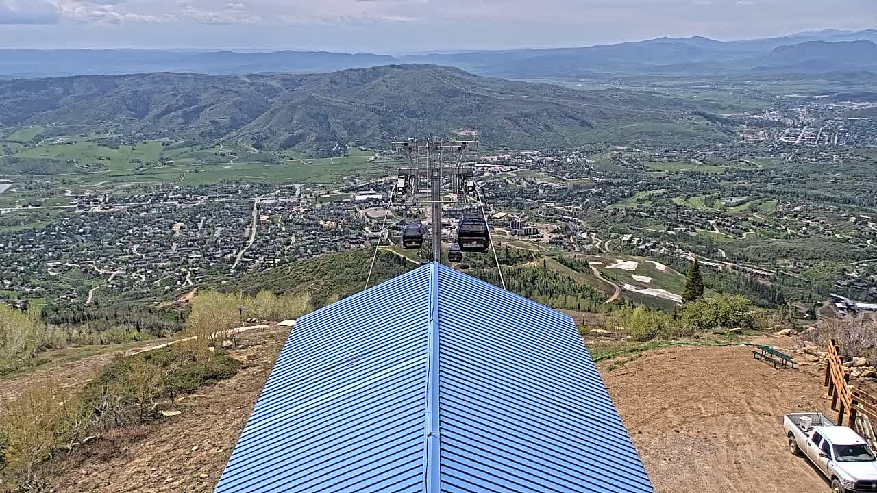 A chairlift ascends a mountain overlooking a valley town under partly cloudy skies.