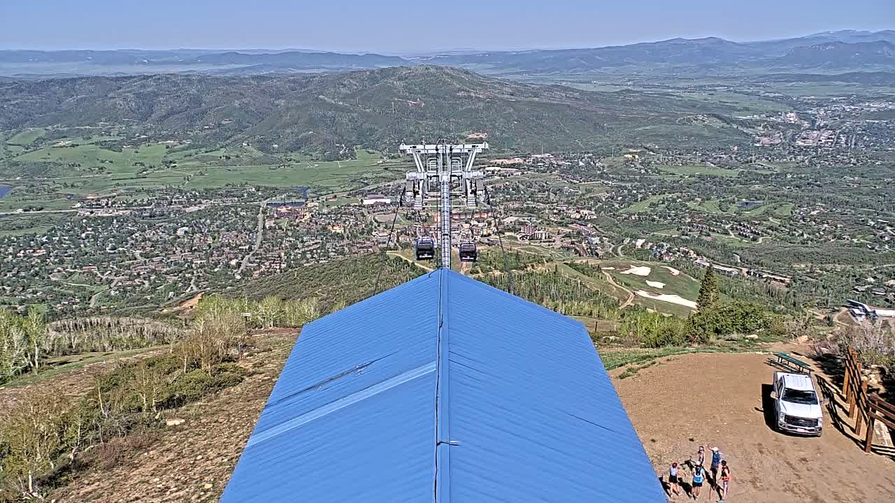 A chairlift ascends a mountain overlooking a sprawling town nestled in a valley on a clear, sunny day.