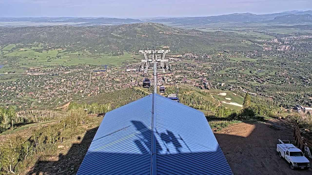 A chairlift ascends a mountain overlooking a sprawling town nestled in a valley on a sunny day.