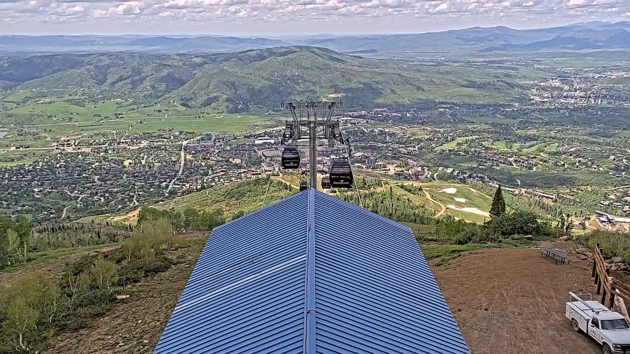 A chairlift ascends a mountain overlooking a valley town under partly cloudy skies.