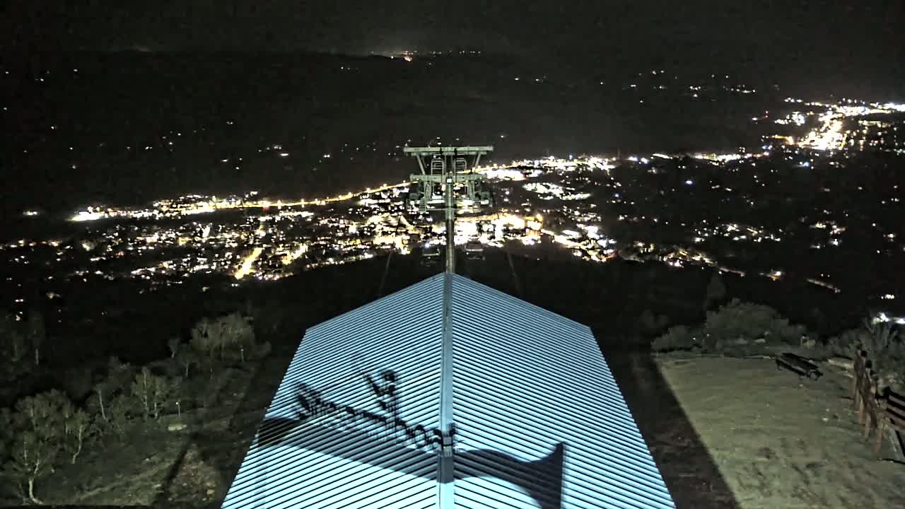 At night, a cable car station sits atop a hill overlooking a brightly lit city sprawling across a valley.