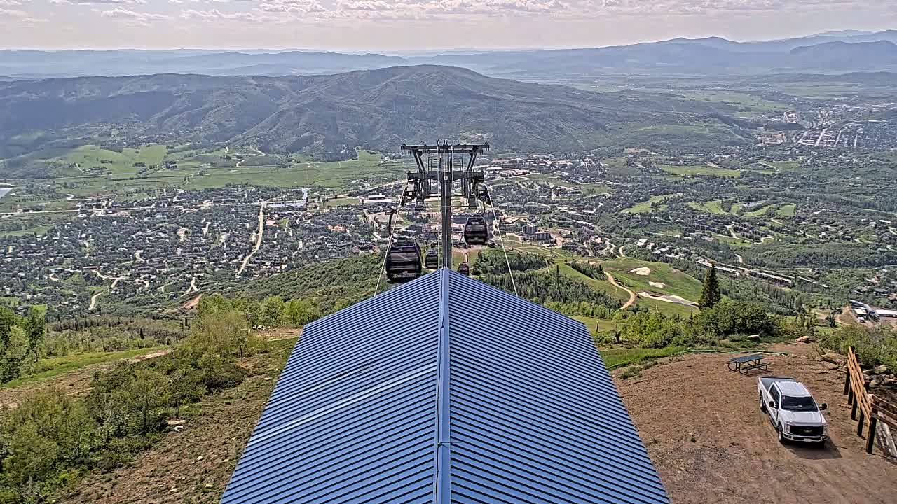 A chairlift ascends a mountain overlooking a town nestled in a valley on a partly cloudy day.