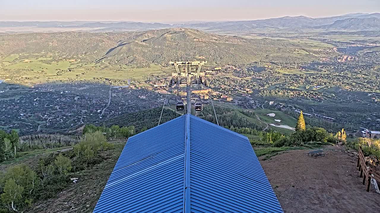 A chairlift ascends a mountain overlooking a valley town under a clear sky.