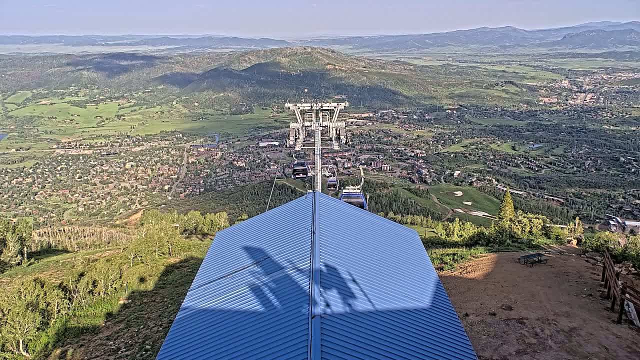 A chairlift ascends a mountain overlooking a valley town under a clear sky.